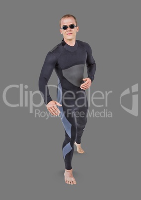 Full body portrait of man in wet suit and goggles standing with grey background