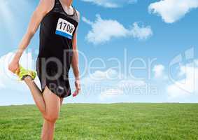 Athlete stretching leg in front of field and sky