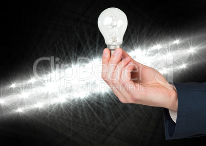 Hand holding bulb in front bright lights and darkness