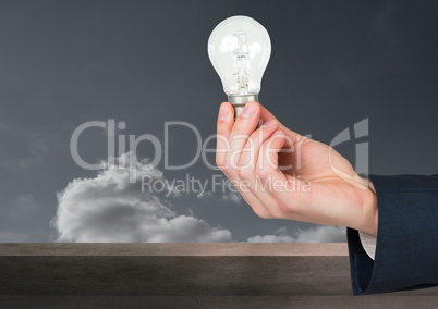 Hand holding light bulb in front of clouds