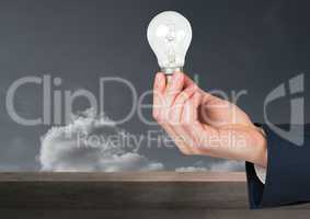 Hand holding light bulb in front of clouds