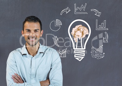 Man standing next to light bulb with crumpled paper ball and business graphics  in front of blackboa