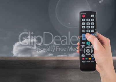 Hand holding tv remote control in front of clouds