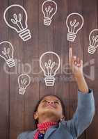 Happy office kid girl pointing up against wood background with bulbs icons