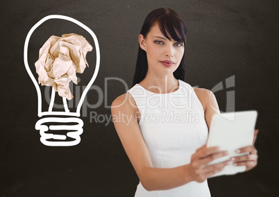 Woman with tablet standing next to light bulb with crumpled paper ball in front of blackboard