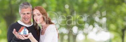 Happy couple holding a house against green background as concept of insurance