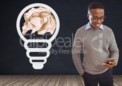 Man on phone standing next to light bulb with crumpled paper ball in front of blackboard