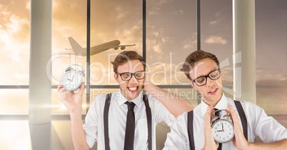 Twin hipster men holding clocks in airport