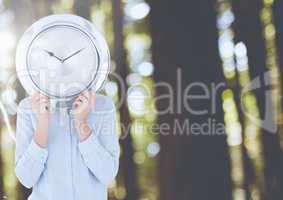 Woman holding clock in front of forest