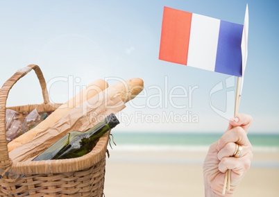 Hand holding French flag with baguettes and wine on beach
