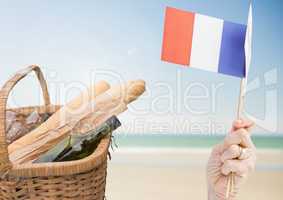 Hand holding French flag with baguettes and wine on beach