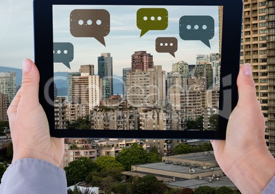 Holding tablet and Chat bubble icons over city