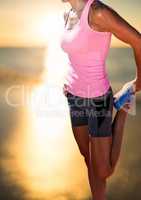 Athlete woman stretching leg in front of sunset over sea