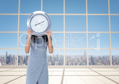 Woman holding clock in front of windows with city skyline
