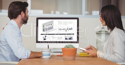 Business people having discussion over graphs on computer monitor in office