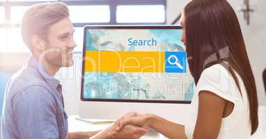 Business people shaking hands while standing by computer with search text