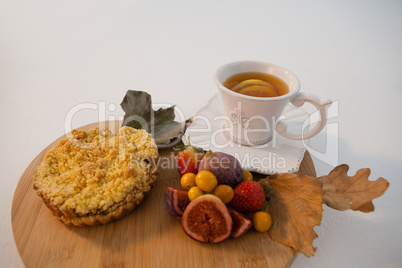 Various fruits, sweet food, autumn leaves and cup of green tea on chopping board