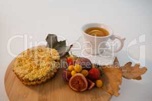 Various fruits, sweet food, autumn leaves and cup of green tea on chopping board