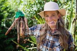Portrait of happy woman holding harvested carrots in field