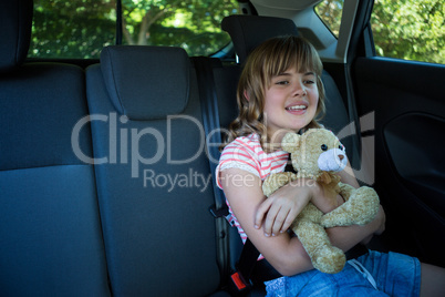 Teenage girl with teddy bear sitting in the back seat of car