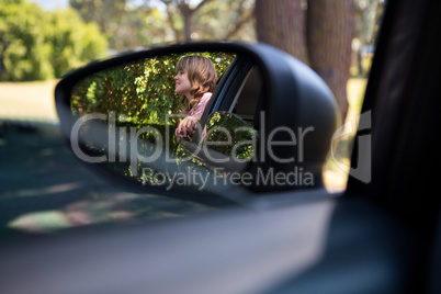 Reflection of teenage girl in wing mirror standing beside a car