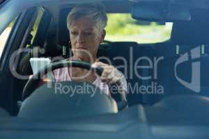 Senior woman using mobile phone while driving car