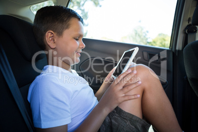 Teenage boy using digital tablet in the back seat of car