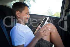 Teenage boy using digital tablet in the back seat of car
