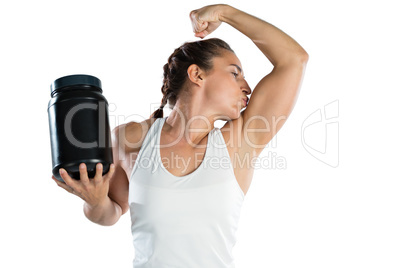 Female athlete holding supplement jar while kissing biceps