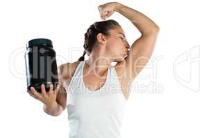 Female athlete holding supplement jar while kissing biceps