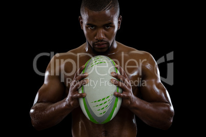 Portrait of shirtless male athlete holding rugby ball