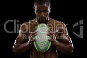 Portrait of shirtless male athlete holding rugby ball