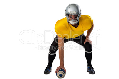 Portrait of American football player wearing helmet bending while holding ball