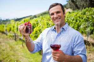 Smiling vintner holding grapes and glass of wine