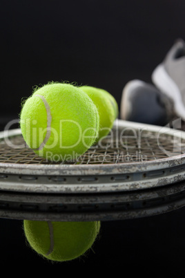 Close up of fluorescent yellow tennis balls on racket by sports shoes with reflection