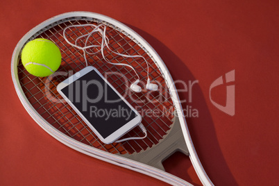 High angle view of mobile phone with in-ear headphones and ball on tennis racket
