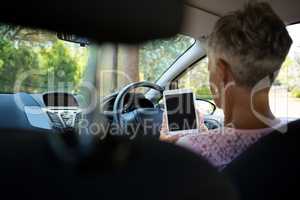 Senior woman using digital tablet while driving a car