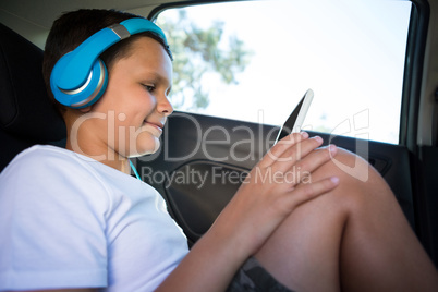 Teenage boy with headphones using digital tablet in the back seat of car