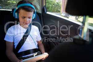 Teenage boy using digital tablet in the back seat of car