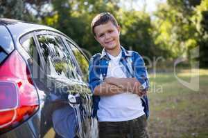 Teenage boy standing with arms crossed near a car