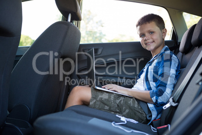 Teenage boy using laptop in the back seat of car