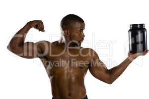 Shirtless male athlete flexing muscles while holding supplement jar