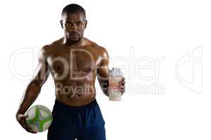 Portrait of shirtless sportsman with rugby ball holding drinking bottle