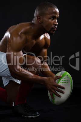 Side view of shirtless sportsman holding rugby ball