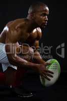 Side view of shirtless sportsman holding rugby ball