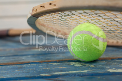 Close up of wooden tennis racket leaning on fluorescent yellow ball