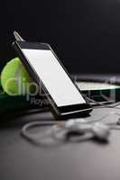 Close up of smartphone and headphones by tennis ball with racket