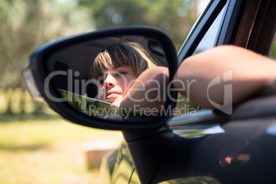Reflection of teenage girl in wing mirror of a car