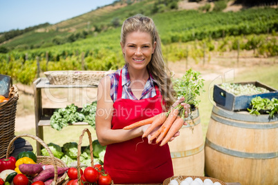 Portrait of happy woman holding fresh carrots at vegetable stall