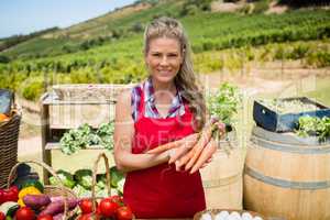 Portrait of happy woman holding fresh carrots at vegetable stall